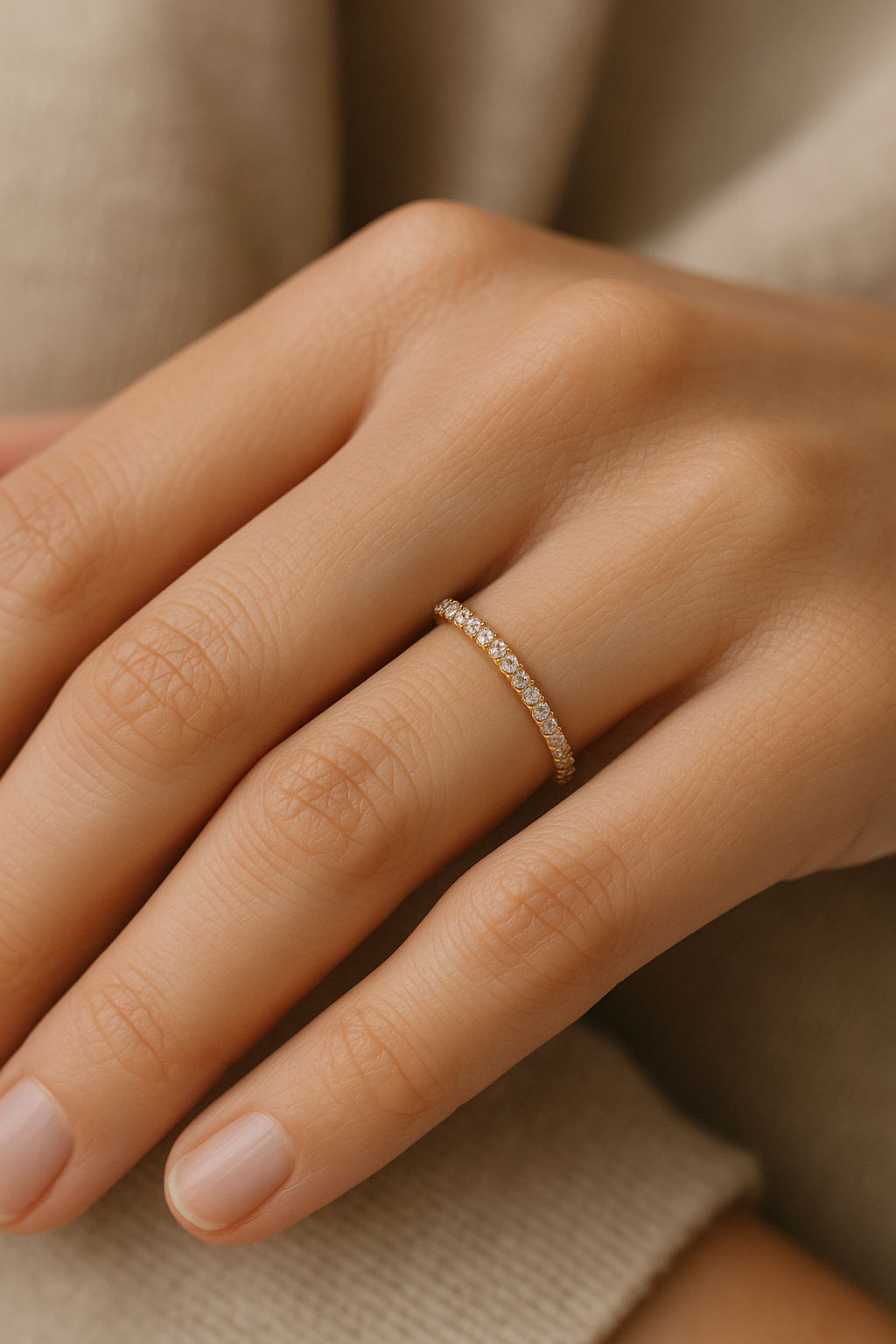 1.5 mm Moissanite Eternity Ring in 14k yellow gold elegantly worn on a model’s hand. The close-up highlights the shimmering moissanite stones encircling the band against her skin and a soft, neutral fabric backdrop.