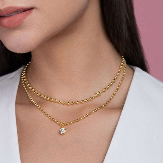 Gold necklace with a small gemstone on a model against a pink background
