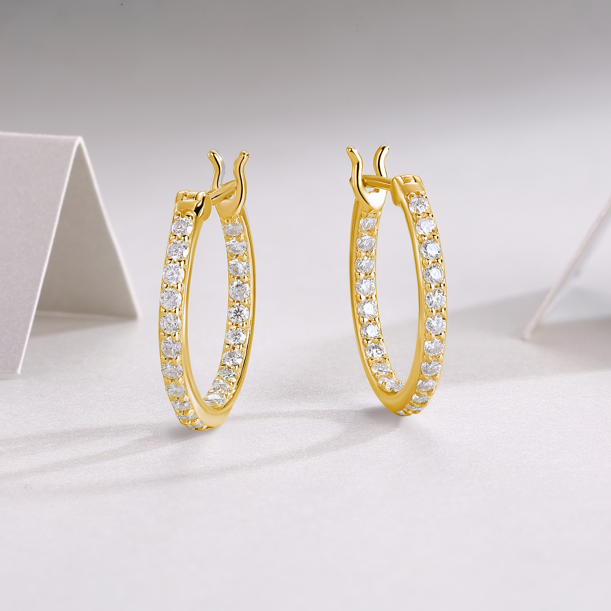 Gold hoop earrings with clear stones on a light gray background