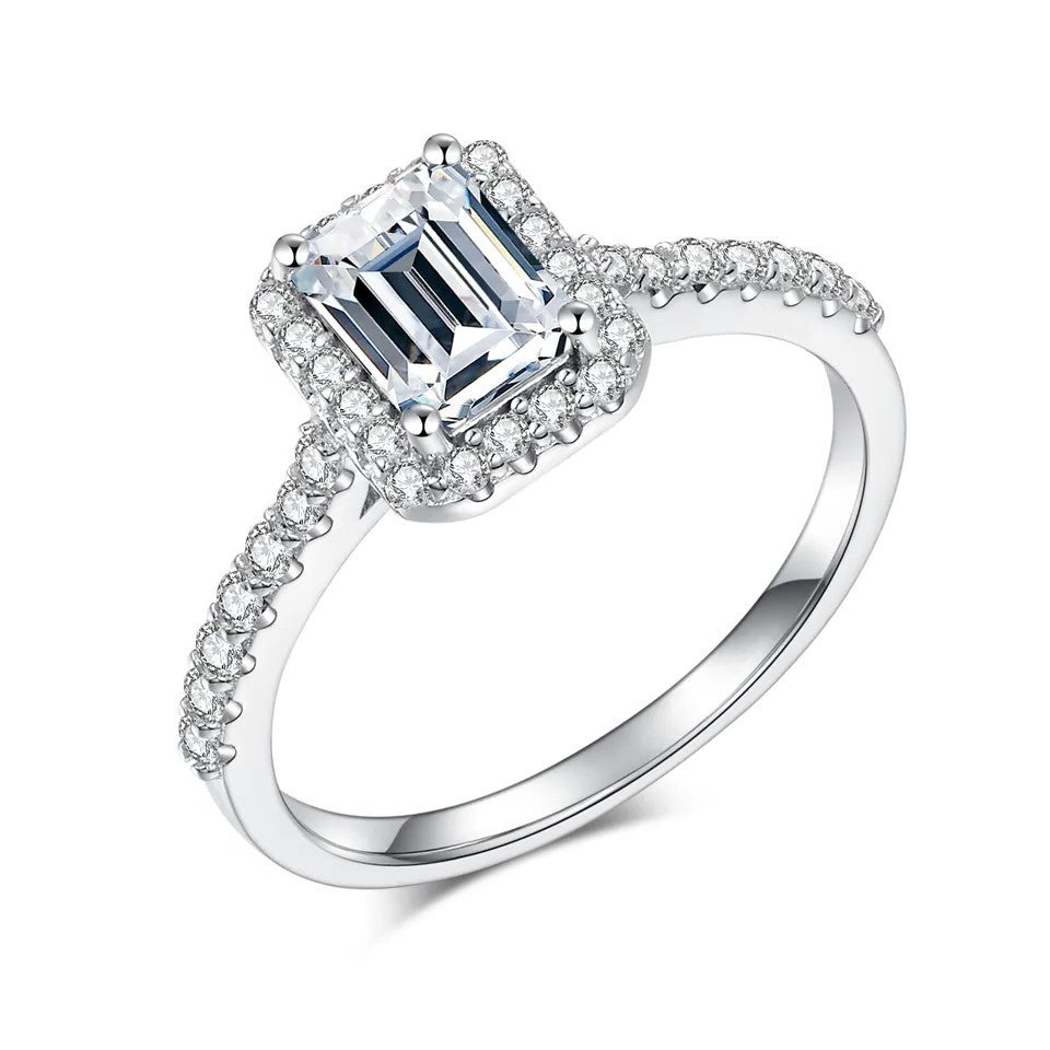 A 1 carat emerald cut halo ring with a half pave band, set in a white gold band.