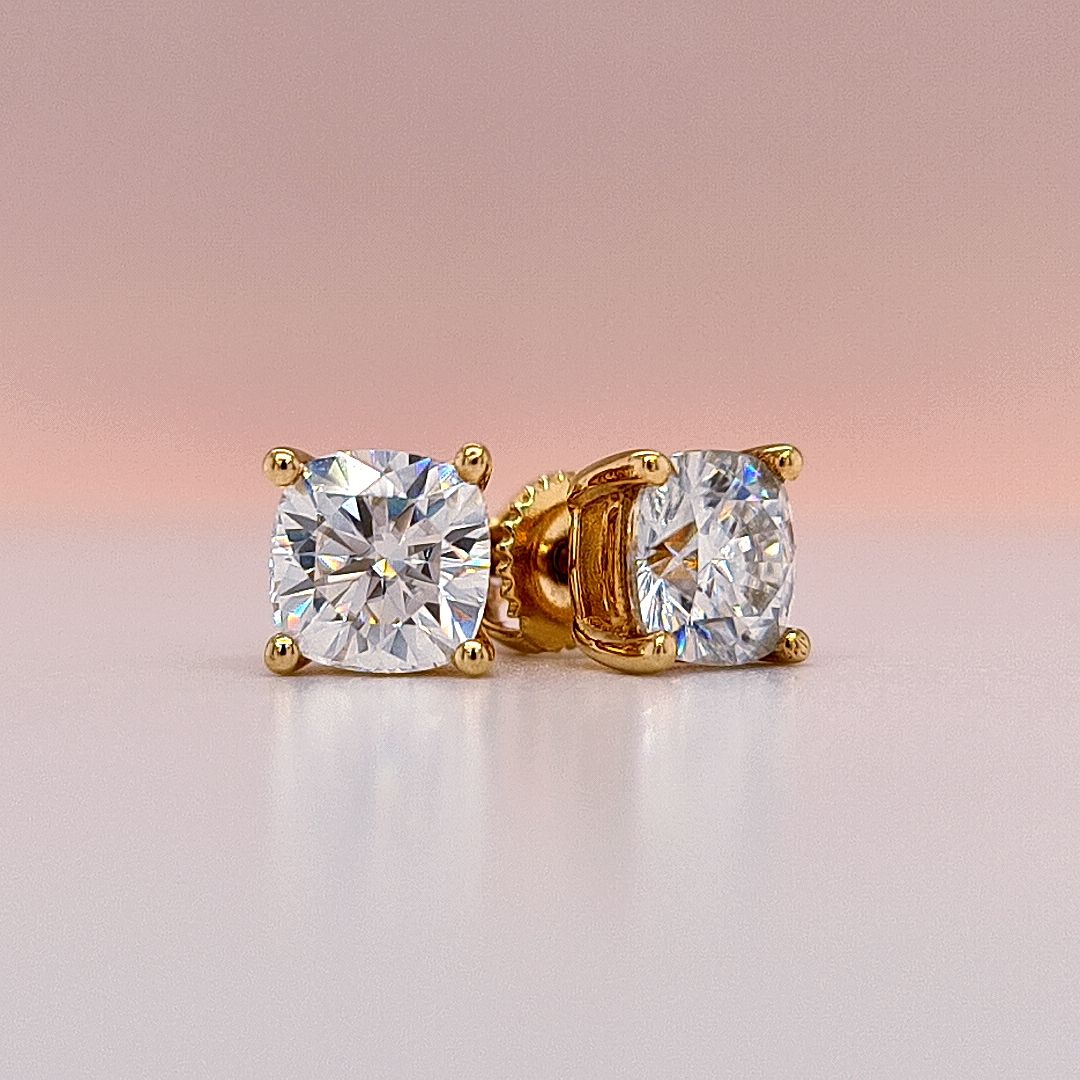 Gold stud earrings with clear cushion cut moissanite diamond gemstones on a white background