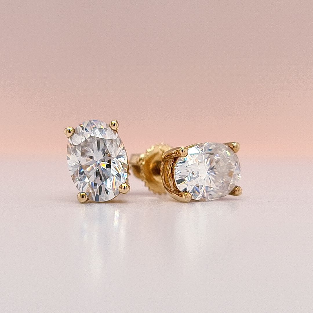 Gold stud earrings with large clear oval cut moissanite diamonds gemstones on a white background
