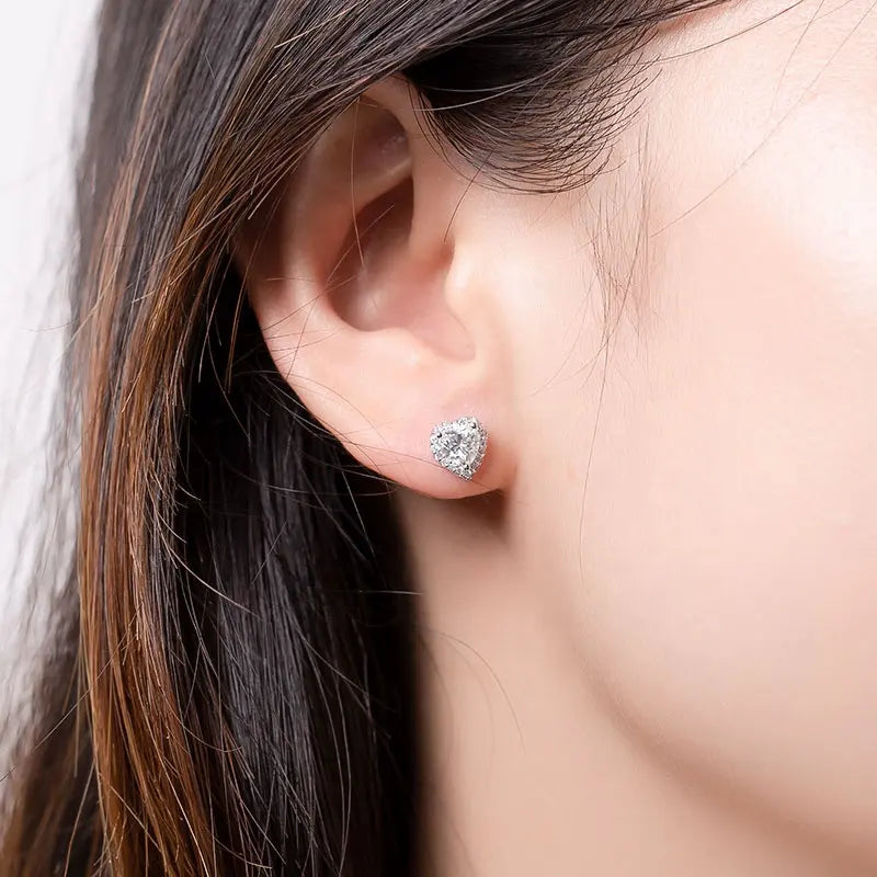 Close up of brunettes ears wearing a 1 carat heart cut moissanite stud with halo in14K gold