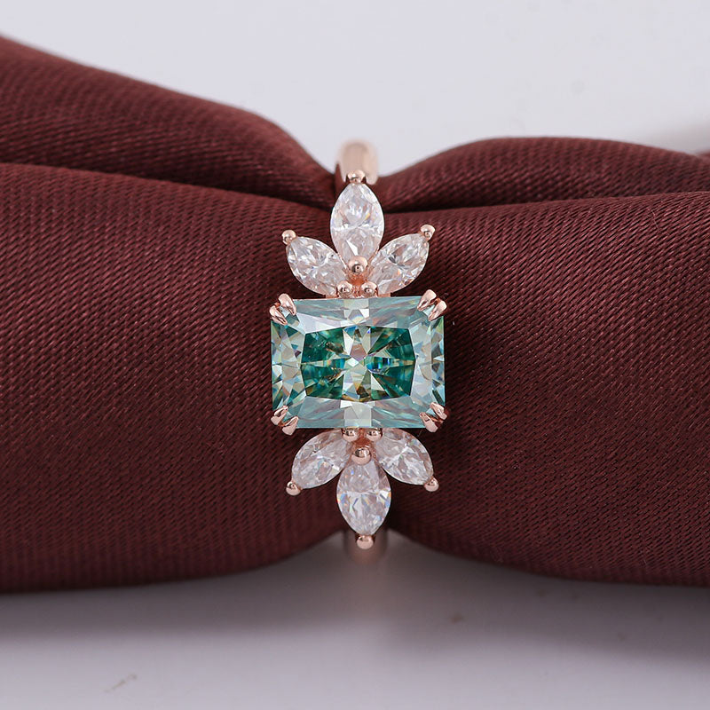 Green radiant cut moissanite and marquise ring on a white and maroon background