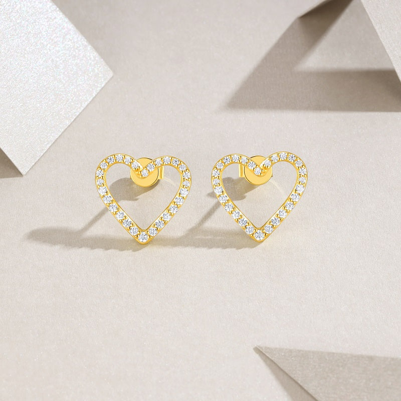 Gold heart-shaped earrings with clear stones on a light beige background