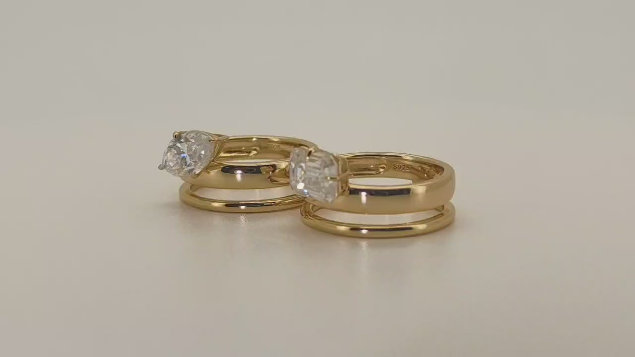 Two gold-plated sterling silver moissanite 2 carat rings displayed side by side on a soft neutral background—one with a marquise-cut stone set east-west, the other with an emerald-cut moissanite. Both styles feature matching plain gold bands beneath the main ring.