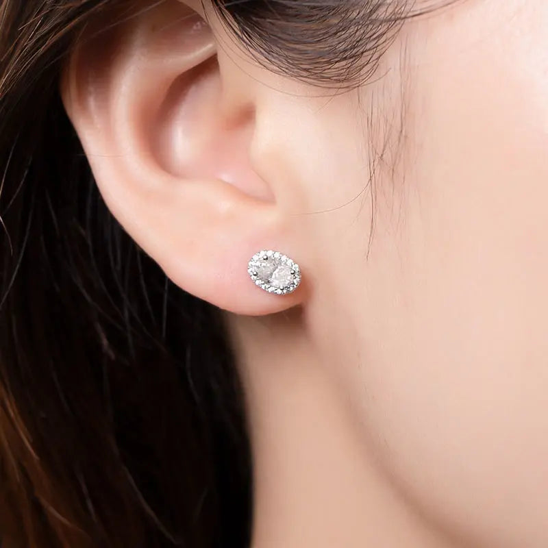 Close up of brunettes ears wearing a 1 carat oval cut moissanite stud with halo in14K gold