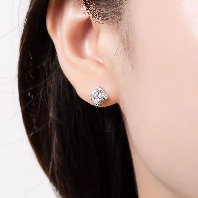 Close up of brunettes ears wearing a 1 carat princess cut moissanite stud with halo in14K gold