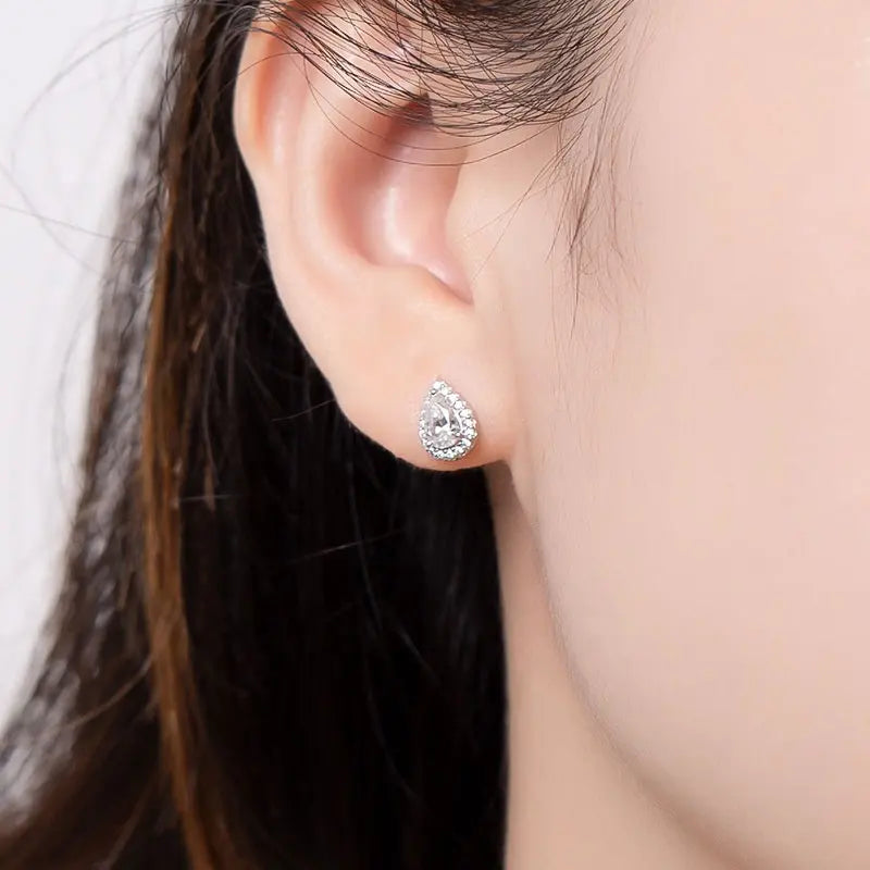 Close up of brunettes ears wearing a 1 carat pear cut moissanite stud with halo in14K gold